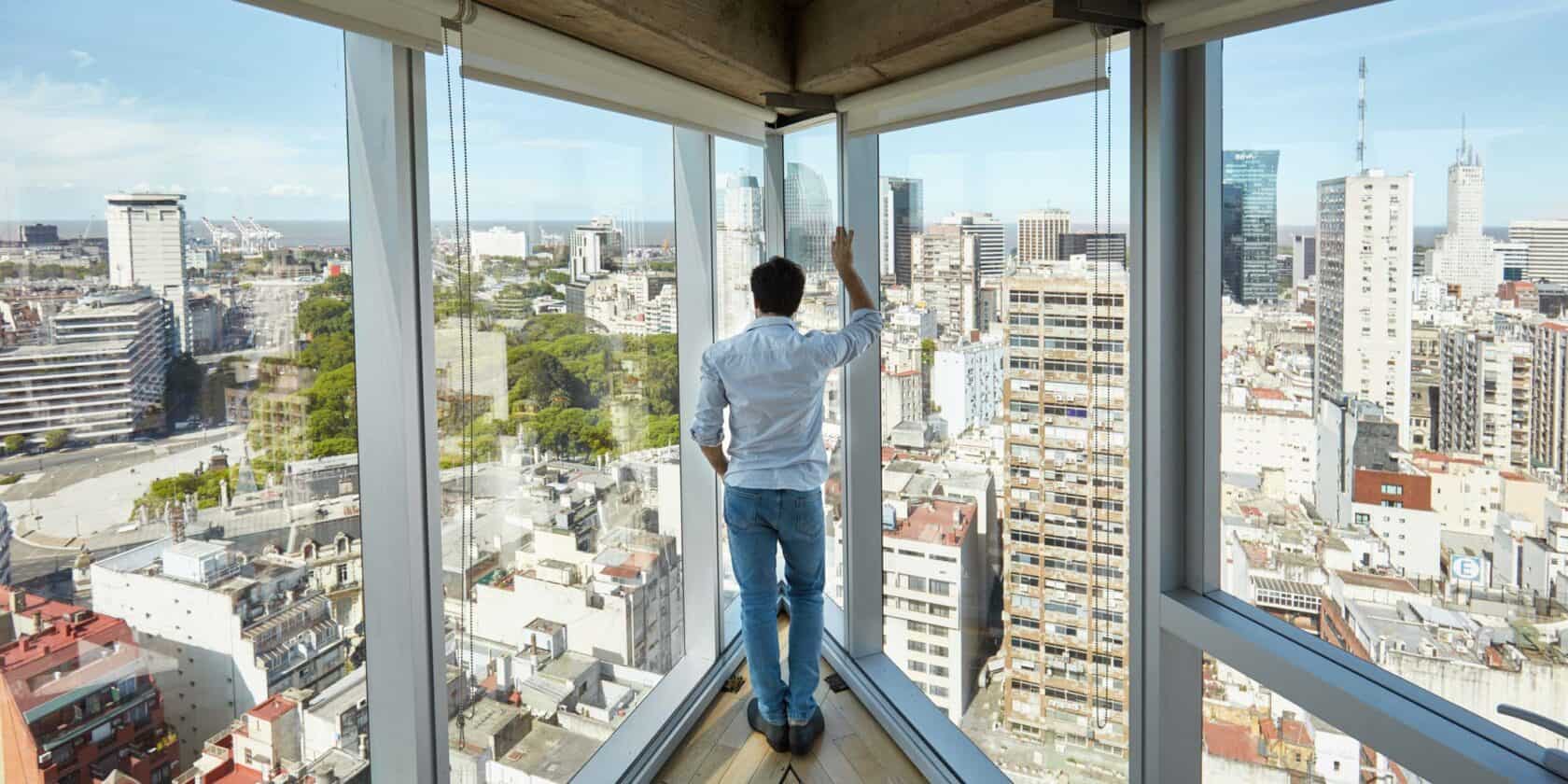 A person looking out glass windows towering over a city.