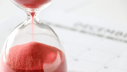 close-up-of-red-sand-slipping-away-through-hourglass-time-running-out-december-calendar-out-of-focus-in-background-end-of-year-no-more-time