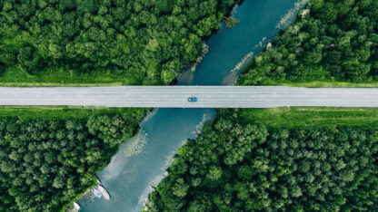 Overhead photo of blue vehicle crossing highway over river in forest.