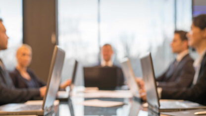 Boardroom meeting with laptops open in front of attendees.