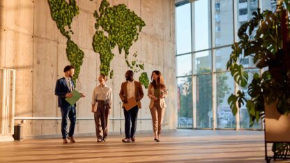 People in business attire walking through an office hallway with natural light.