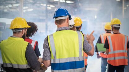 Back side of engineers, technician and workers team in safety uniform having discussion while walking through heavy industry manufacturing factory
