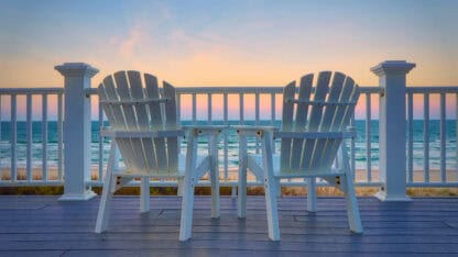 Adirondack chairs on the balcony deck of a house looking out over the beach and ocean