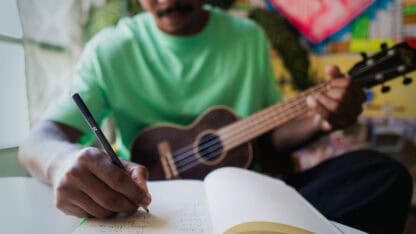 Musician composing a song playing and writing lyrics in notebook