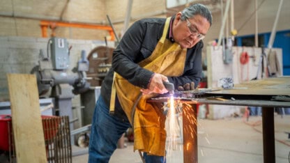 Man using a welder on a piece of steel in a metal workshop