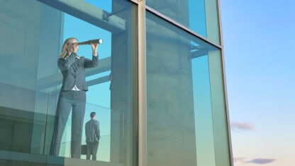 Businessperson looking out from glass building with telescope, representing how SOC 1 reports can help you better see what's going on with third-party vendors and increase your audit readiness