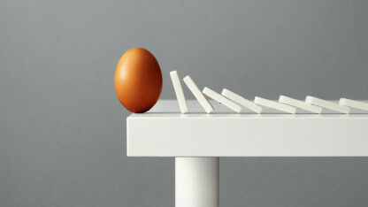 Image of dominos and an egg on the edge of a table representing how ERISA plan forfeiture accounts must be used within IRS timelines to adhere to retirement plan compliance
